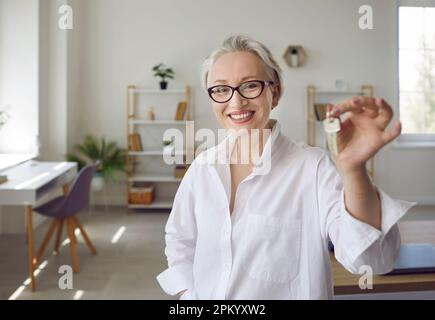 Porträt einer glücklichen, reifen Frau, die Schlüssel zu ihrem neu gekauften Haus hält und lächelt Stockfoto