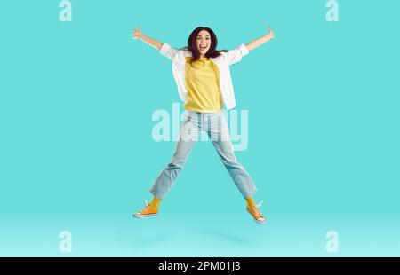 Fröhliche, lustige Frau springt fröhlich und spreizt Arme und Beine auf leuchtend hellblauem Hintergrund. Stockfoto