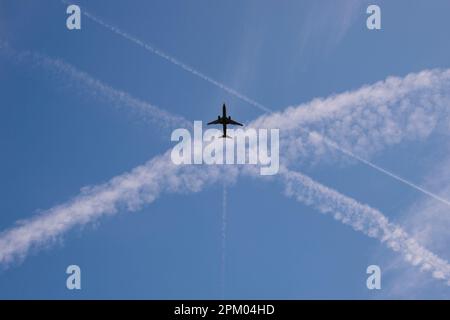 Flugzeug in blauem Himmel mit überquerenden Dampfpfaden Stockfoto