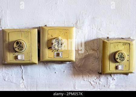 Falsch ausgerichtete alte verschmutzte Schalter zur ein-, aus- und Drehzahlsteuerung von Deckenventilatoren an einer weißen Wand, kleinen gelben Kunststoffkästen, raue strukturierte Wand Stockfoto