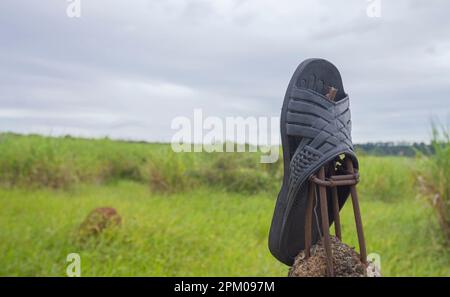 Hausschuhe auf einem Zaun mit Vegetation im Hintergrund an einem bewölkten Tag, Konzept der Umweltverschmutzung der Natur. Stockfoto