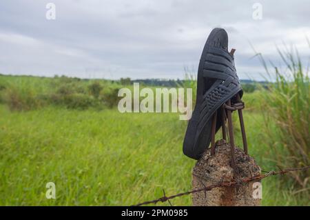 Hausschuhe auf einem Zaun mit Vegetation im Hintergrund an einem bewölkten Tag, Konzept der Umweltverschmutzung der Natur. Stockfoto