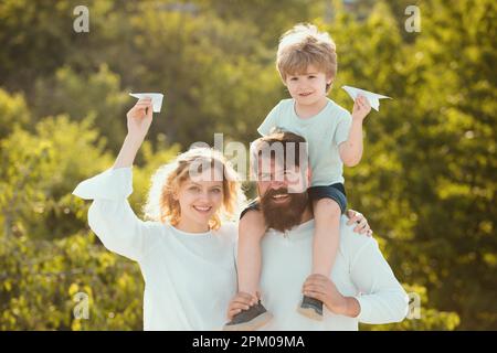 Familienreise und Urlaubskonzept. Vater trägt seinen Sohn auf den Schultern. Elternschaft und Kindheitskonzept. Kinder, die mit einfachen Papierflugzeugen spielen Stockfoto