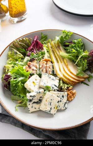 Gesunder Salat aus grünen Salatblättern, Ruckelsalat, Scheiben frischer Birnen, Stücke Blauschimmelkäse, Walnüsse und Sesamsamen. Stockfoto