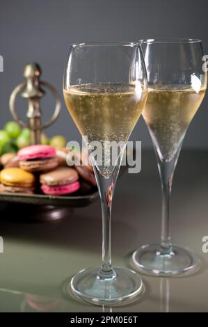 Gläser Sekt, Sekt, Brut oder Cava mit Blasen und süßem Dessert, bunte Makronen-Kekse im Hintergrund Stockfoto