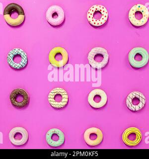 Runde Donuts mit verschiedenen Dekorationen auf einem einfarbigen violett-pinkfarbenen Hintergrund Stockfoto