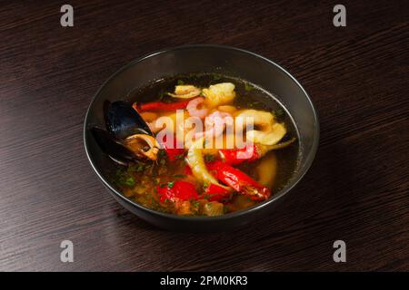 Appetitlich aussehende Meeresfrüchte-Suppe mit Muscheln, Garnelen, roten Paprika auf einem Teller auf einem Holztisch Stockfoto