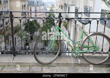 Paris, Frankreich, 29. Oktober 2022: Ein altes grünes Motobecane-Fahrrad neigt sich gegen ein Geländer auf einer abfallenden Straße im historischen Viertel Montmartre Stockfoto