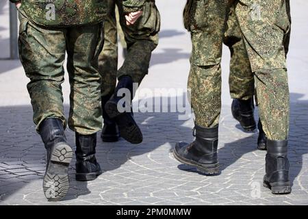 Beine von Soldaten der Streitkräfte in Tarnung, Männer in Stiefeln, die die Straße entlang laufen Stockfoto