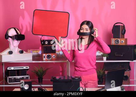 Lächelnder Künstler mit roter Sprechblase, der Textnachrichten aus Pappe im Studio auf pinkfarbenem Hintergrund anbietet. Asiatischer Musiker, der auf einer professionellen Mixerkonsole Melodien erzeugt Stockfoto