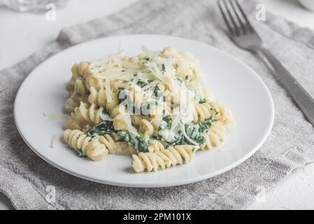 Fusilli Pasta mit Spinat und Ricotta garniert mit geriebenem Parmesan Käse auf weißem Teller Stockfoto