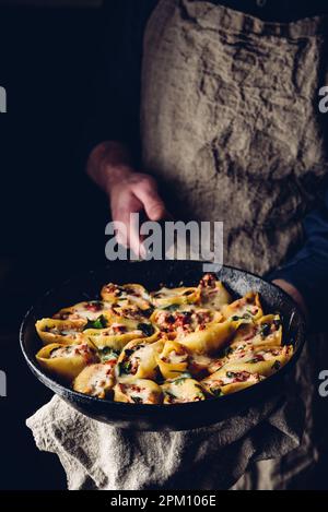 Der Küchenchef hält eine Pfanne mit gebackenen Jumbo-Shells-Pasta, gefüllt mit Hackfleisch, Spinat und Käse Stockfoto