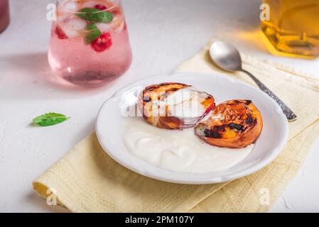 Serviert mit Honig gebackene Pfirsiche auf weißem Teller mit Schlagsahne und einem Glas Himbeere und Minze Cocktail Stockfoto