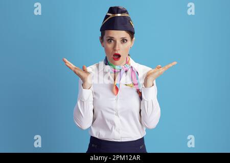 Überraschend stilvolle Stewardess mit blauem Hintergrund in Uniform. Stockfoto