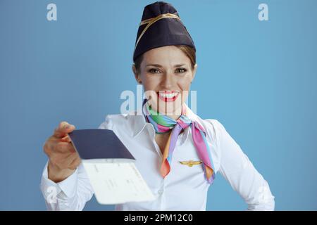 Lächelnde, stilvolle Stewardess isoliert auf blauem Hintergrund in Uniform mit Flugtickets und Pass. Stockfoto