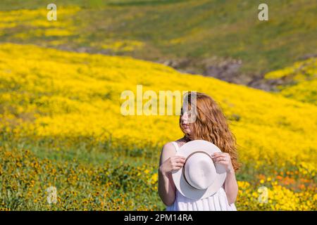 Eine Frau, die den Frühling auf einer wunderschönen Wiese voller leuchtend gelber Wildblumen genießt. Stockfoto