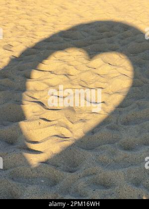 Überbleibsprojektion herzförmiger Strukturschatten auf Strandsand mit zahlreichen Fußabdrücken. Stockfoto