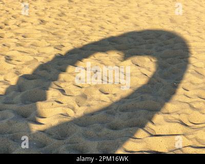 Überbleibsprojektion herzförmiger Strukturschatten auf Strandsand mit zahlreichen Fußabdrücken. Stockfoto