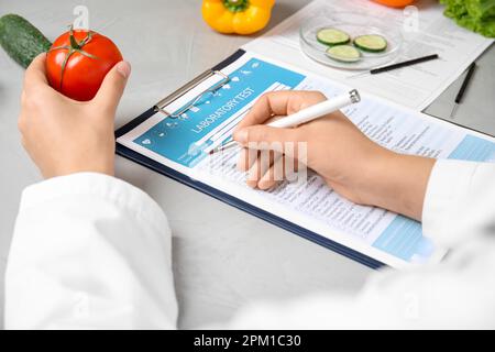 Wissenschaftler mit Labortestform und frischer Tomate am Tisch im Haus, Nahaufnahme. Gifterkennung Stockfoto