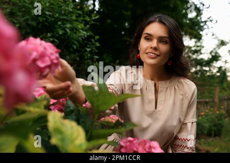 Eine schöne Frau, die ein gesticktes Kleid im blühenden Garten trägt. Ukrainische Nationalkleidung Stockfoto