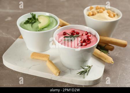 Verschiedene köstliche Hummusen mit Brotstangen auf einem braunen Marmortisch Stockfoto