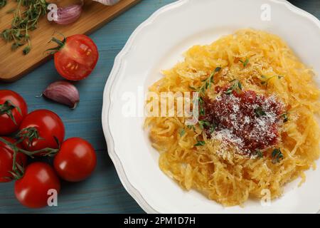 Leckerer Spaghetti-Kürbis mit Tomatensoße, Käse und Thymian, serviert auf einem hellblauen Holztisch, flach liegend Stockfoto