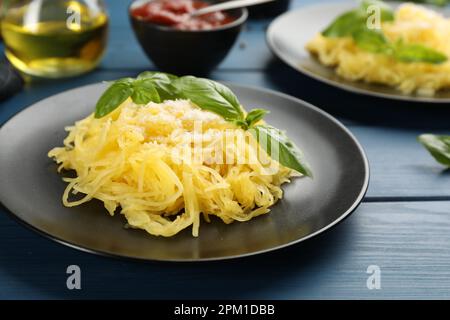 Leckerer Spaghetti-Kürbis mit Basilikum und Käse, serviert auf einem blauen Holztisch, Nahaufnahme Stockfoto