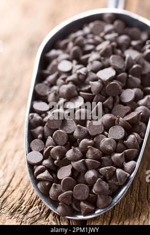 Schokoladenstücke oder Leckereien in Metallschaufel auf Holz (Selektive Fokussierung, Fokus auf ein Drittel der Schokoladenstücke) Stockfoto