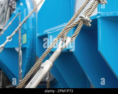 Drahtseil mit Spannschlössern und Klemmen, das schwere Maschinen für den Versand an Ort und Stelle hält. Geringe Schärfentiefe mit fokussiertem Vordergrunddraht. Stockfoto