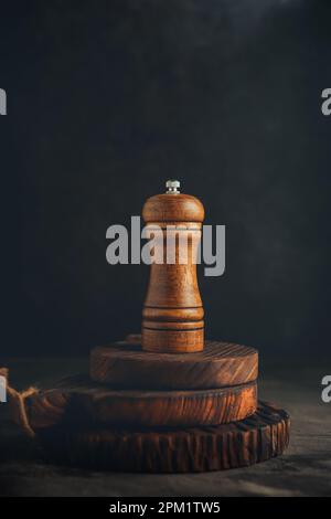Pfeffermühle aus Holz auf rustikaler Holzuntersetzer und abstraktem Hintergrund Stockfoto