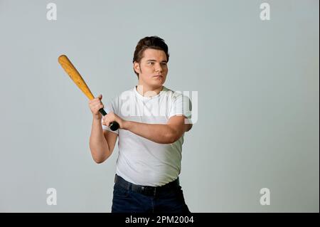 Ein Mann mit einem Schläger in der Hand schwingt auf grauem Hintergrund Stockfoto
