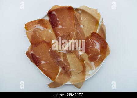 Scheiben von italienischem Prosciutto di parma, italienischem Schinken, in einem weißen Gericht isoliert auf Weiß. Draufsicht Stockfoto