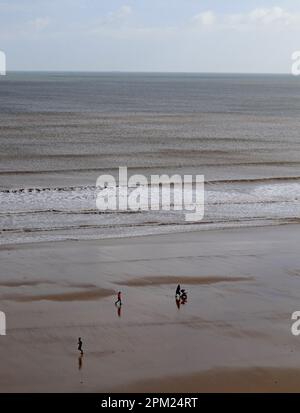 Die Flut geht los, sodass ein Paar seinen Jungen in einem Liegestuhl entlang des ruhigen Hunmanby Sands laufen kann, während jemand in die andere Richtung joggt Stockfoto