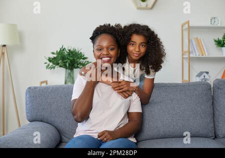 Porträt von frohen afroamerikanischen Mutter und Tochter, die sich umarmen, in die Kamera schauen und lächeln Stockfoto