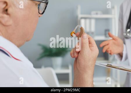 Seniorpatient mit Schwerhörigkeit mit einem modernen Hörgerät, das ihm der Arzt gegeben hat Stockfoto