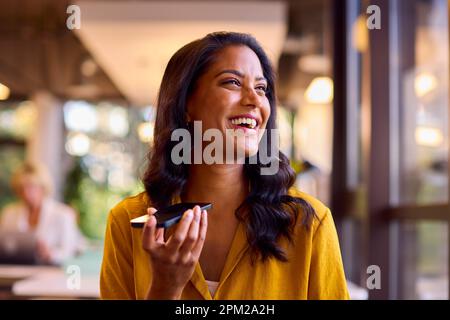 Eine Ältere Geschäftsfrau, Die Am Schreibtisch Arbeitet Und Sich Mit Dem Mikrofon Des Mobiltelefons Unterhält Stockfoto