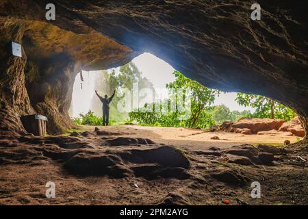 Rückansicht eines Mannes in einer Höhle vor einem Wasserfall in Sipi Falls, Kapchorwa, Uganda Stockfoto