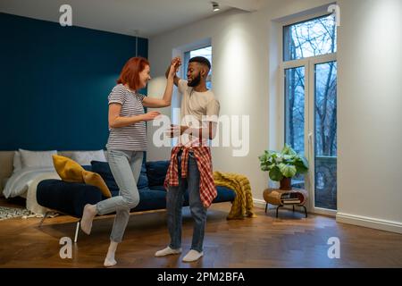 Liebevolles junges, vielfältiges Paar, das romantischen Tanz im modernen Schlafzimmer mit Panoramafenstern tanzt. Stockfoto