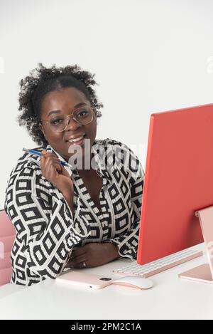England, Großbritannien. 2022. Glückliche lächelnde Frau, die an einem Desktop-Computer arbeitet und in die Kamera schaut. Stockfoto