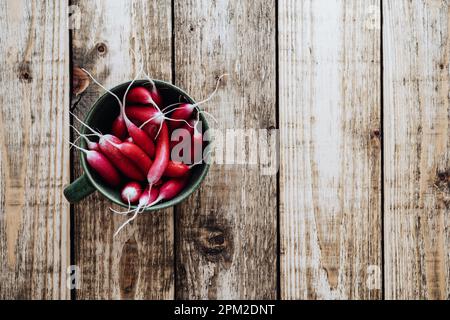 Langes Frühstück Radieschen in Keramikschale auf Holzbrett von oben gesehen. Frisches, im Frühling angebautes Bio-Gemüse, gesunde vegane Lebensmittel auf Pflanzenbasis Stockfoto