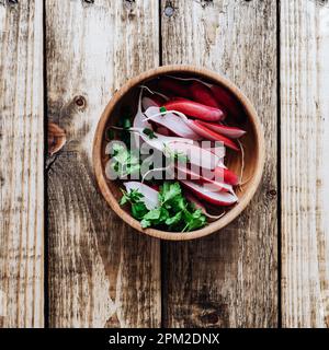 Langes Frühstück Radieschen in Keramikschale auf Holzbrett von oben gesehen. Frisches, im Frühling angebautes Bio-Gemüse, gesunde vegane Lebensmittel auf Pflanzenbasis Stockfoto