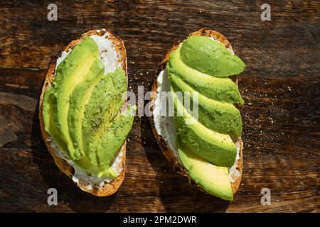 Zwei Vollkorntoasts mit Avocado-Scheiben auf rustikalem Holzbrett. Mexikanische Küche, aus nächster Nähe, Blick von oben Stockfoto