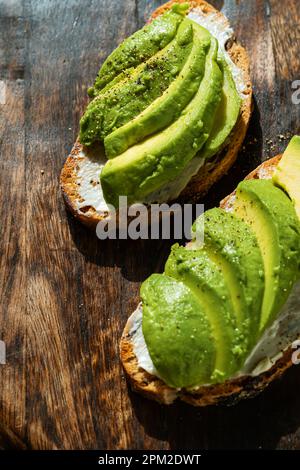 Zwei Vollkorntoasts mit Avocado-Scheiben auf rustikalem Holzbrett. Mexikanische Gerichte, aus nächster Nähe Stockfoto