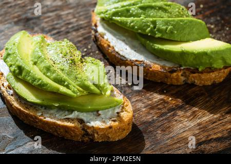 Zwei Vollkorntoasts mit Avocado-Scheiben auf rustikalem Holzbrett. Mexikanisches Essen, Nahaufnahme Stockfoto