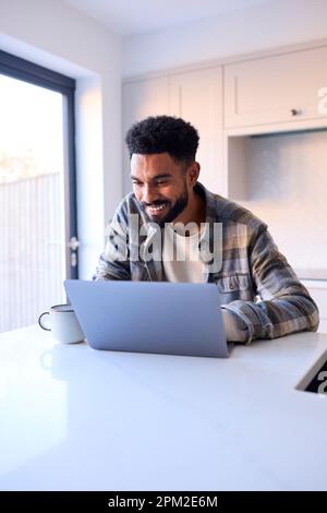 Mann Zu Hause, Der An Einem Laptop An Der Theke In Der Küche Arbeitet Stockfoto