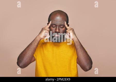 Ein afroamerikanischer Mann, der über eine neue Idee nachdenkt und seinen Kopf mit Händen vor braunem Hintergrund hält Stockfoto