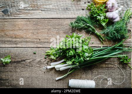 Frische Bio-Kräuter und Gemüse zum Kochen auf einem rustikalen Küchentisch von oben. Grüne Zwiebel, Dill, Petersilie, Knoblauch auf Holzhintergrund Stockfoto