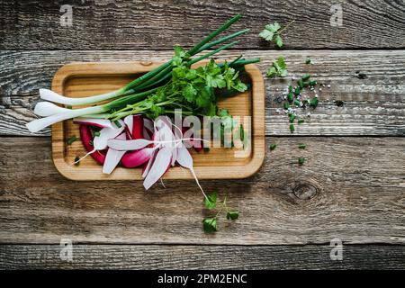 Frische Bio-Kräuter und Gemüse zum Kochen auf einem rustikalen Küchentisch von oben. Grüne Zwiebel, Petersilie, Rettich auf Holzhintergrund Stockfoto