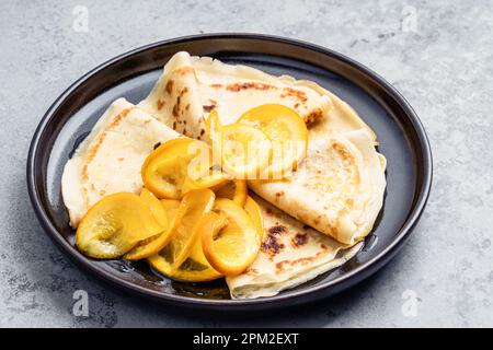 Teller mit Crepes mit orangefarbenem auf grauem Hintergrund, Nahaufnahme... Crepes Suzette Stockfoto