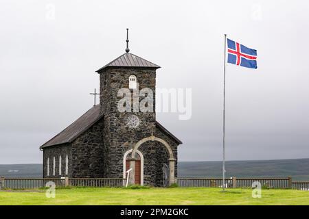 Landschaft mit sehr alter Steinkirche Thingeyrak (Thingeyrakirkja) in Island mit einer Flagge im Wind Stockfoto